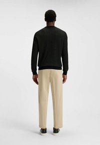 Svart mönstrad tröja med rund hals, tillsammans med beige byxor och svarta sneakers. Tröjan har en strukturerad herringbone-design.