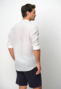 Witte linnen shirt met oprolbare mouwen, casual fit, gebogen zoom, gecombineerd met marineblauwe shorts, gezien vanuit de achterkant.