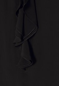 Zwarte stof met laagjes ruches met fijne, licht glanzende randen tegen een matte zwarte achtergrond.