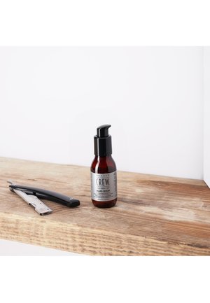 Bouteille en verre marron avec un bouchon-pompe noir, étiquetée "Sérum à Barbe", à côté d'un rasoir métallique et d'un manche noir, sur une surface en bois.