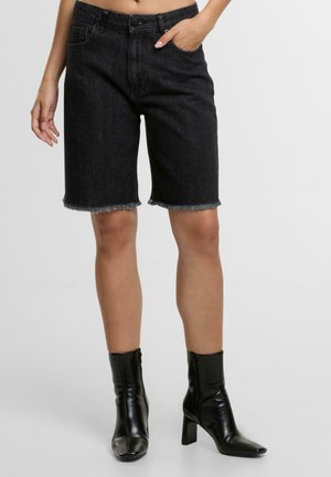Shorts de mezclilla negra con dobladillo deshilachado, cintura alta y bolsillos frontales, combinados con botas negras hasta el tobillo con tacón cuadrado y cierre de cremallera.