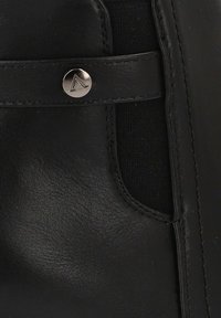 Bota de cuero negra con una textura suave, que presenta un panel elástico lateral y un acento metálico del logo cerca del cierre de botón.