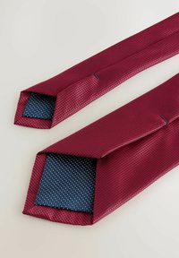 Burgundy tie with a textured surface; inner side features a navy blue pattern with small dots. Ends are pointed and neatly finished.