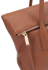 Sac à main en cuir brun texturé avec un dessus zippé, un design plat, et des accents en métal doré, comportant deux poignées supérieures et une poche latérale.