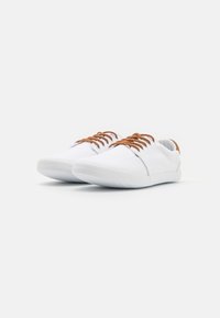Baskets en toile blanches avec des lacets marron, bout rond, texture lisse et design minimaliste ; comprend une semelle en caoutchouc légère et flexible.