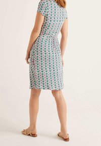 Jurk met korte mouwen in een groen, roze en wit bloemenpatroon, met een getailleerde taille en een zoom tot op de knie; gedragen met beige sandalen.