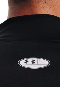 Svart treningstrøye med en sirkulær etikett på baksiden med en hvit Under Armour-logo og plass til navn og nummer.