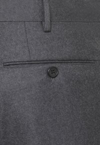 Pantaloni grigi su misura con una texture liscia, una tasca frontale con un bottone decorativo nero e dettagli di cucitura sottili.