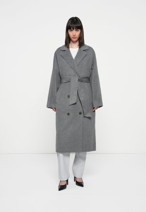 Gray wool wrap coat featuring a double-breasted design, wide lapels, tie waist, and large buttons. Worn over light gray trousers and heels.