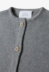 Grauer gestrickter Cardigan mit rundem Halsausschnitt, ausgestattet mit zwei beigen Knöpfen und einem Stoffetikett mit Text. Weiche Textur und engmaschiges Design.