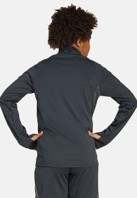 Veste de sport à manches longues en tissu gris foncé. Dotée d'un col haut, d'une coupe ajustée et de panneaux en maille sur les côtés pour la respirabilité.