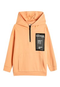 Sudadera de color durazno hecha de tela suave, con un cierre de media cremallera en el frente, un bolsillo frontal y un parche de diseño gráfico negro en el pecho.