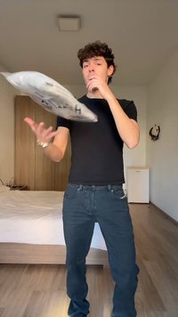 Ung mann i svart skjorte kaster en tett grå pakke i et sparsommelig møblert soverom.