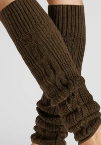 Gestrickte Beinstulpen in Dunkelbraun mit einem gerippten und strukturierten Muster. Weicher Stoff mit gerafften Abschnitten für eine figurbetonte Passform.