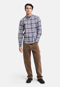 Karierte Hemd mit Knöpfen in Blau, Weiß und Rosa; beige Cordhosen; schwarze Schuhe. Slim Fit, lange Ärmel mit Kragen.