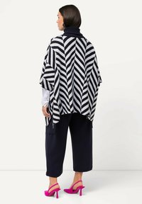 Poncho a righe blu e bianche con colletto alto, abbinato a pantaloni scuri e tacchi rosa. Il design presenta un motivo a zigzag e una texture morbida.