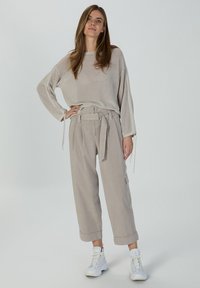 Beige knit sweater with wide sleeves, paired with light beige cargo pants featuring a tied waist, rolled cuffs, and white sneakers.