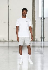 Witte t-shirt met korte mouwen en logo, grijze shorts en witte sneakers. Glad katoenmateriaal, ontspannen pasvorm, eenvoudig ontwerp.