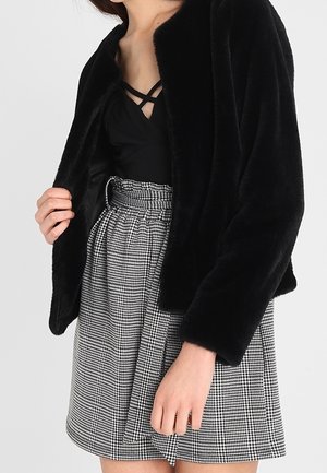 Woman wearing a black faux fur jacket over a black strappy top with a high-waisted black-and-white houndstooth skirt.