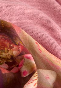 Roze gebreide stof overlapt met een zijdeachtige textiel met bloempatroon, gekenmerkt door zachte kleuren en een gladde textuur.