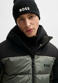 Black beanie with "BOSS" logo, grey and black puffer jacket with zip front and hood, textured fabric, high collar, tight fit.