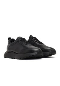 Sneakers neri in pelle con pannelli testurizzati, punta rotonda, chiusura con lacci nella parte frontale e una suola in gomma spessa con un battistrada stampato.