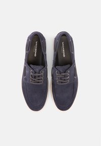 Ζευγάρι απλών παπουτσιών δέτου από ναυτικό μπλε σουέντ με λευκές σόλες, μάρκας "Vagabond", φαίνεται από πάνω σε ανοιχτό φόντο.