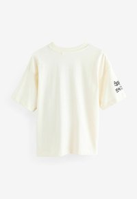 Cremefarvet bomulds t-shirt med korte ærmer og rund hals. Har sort trykt tekstdetalje på højre ærme.