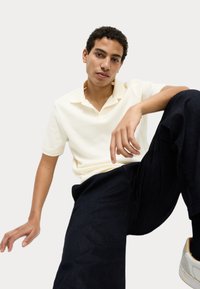 Kortærmet, lys gul polo skjorte med et tekstureret mønster, parret med mørke bukser, som viser en afslappet pasform og et casual design.
