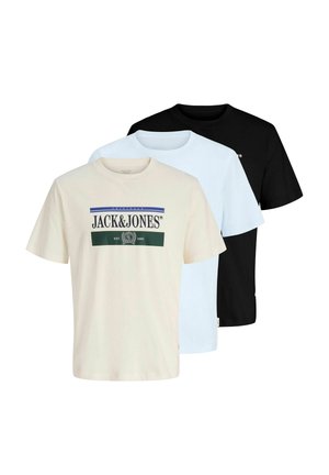 Trois t-shirts à manches courtes pliés en crème avec logo, bleu clair et noir, disposés en chevauchement sur un fond blanc.