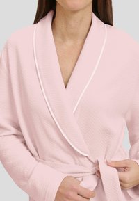 Bata de baño rosa con un patrón de espiga texturizado, ribete blanco en contraste alrededor del cuello en chal y cintura ajustada.