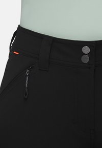 Svarta byxor med en dragkedjeficka, kontrasterande orange accent och silverknappar. Tillverkade av ett strukturerat, töjbart material.