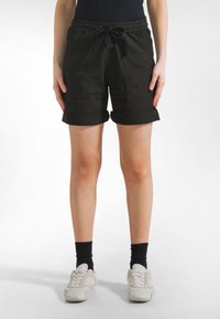 Schwarze Baumwollshorts mit umgeschlagenen Säumen, elastischem Bund und Kordelzug. Mit Seitentaschen und lockerem Sitz. Kombiniert mit weißen Sneakern.