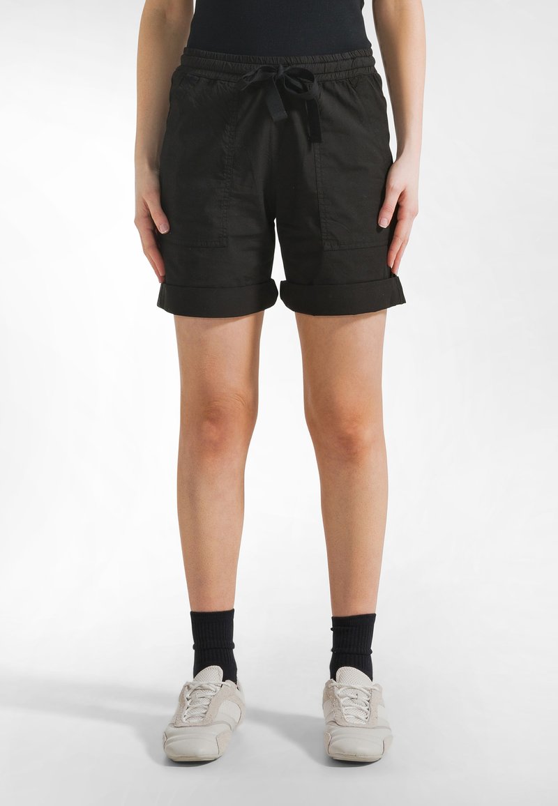 Schwarze Baumwollshorts mit umgeschlagenen Säumen, elastischem Bund und Kordelzug. Mit Seitentaschen und lockerem Sitz. Kombiniert mit weißen Sneakern.