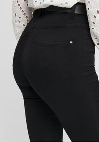 Jeans skinny de tiro alto negros con una textura suave, que cuentan con dos bolsillos traseros y un pequeño detalle metálico cerca del bolsillo derecho.