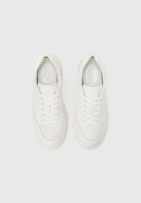 Λευκά αθλητικά παπούτσια με ανάγλυφη υφή, στρογγυλεμένη μύτη, κλείσιμο με κορδόνια, ελαφρώς ανυψωμένη ελαστική σόλα και επενδυμένη γλώσσα για άνεση.