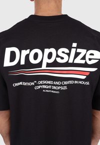 Black cotton t-shirt featuring large white text "Dropsize" and additional text in smaller font. Smooth texture with a relaxed fit design.