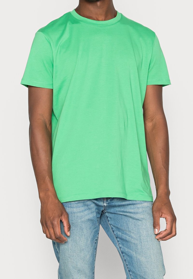 T-shirt in cotone verde con scollo rotondo, maniche corte e vestibilità rilassata. Il tessuto appare liscio, senza motivi o decorazioni.