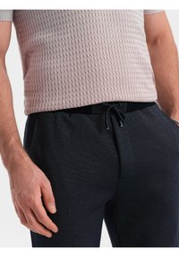 Vaaleanpunainen teksturoitu neulepaita lyhyillä hihoilla, yhdistetty tummansinihin housuihin, joissa on naru vyötäröllä ja hienovarainen kudontakuvio.