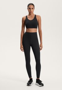 Čierny športový crop top v kombinácii s čiernymi legínami so zvýšeným pásom, vyrobený z hladkého, elastického materiálu. Disponuje minimálnym dizajnom a bezšvovými akcentmi.