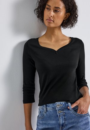 Haut noir à manches longues avec un col rond et un détail à deux boutons, associé à un jean en denim avec un délavage bleu et des accents de boutons.