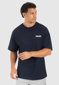 Camiseta de algodón azul marino con mangas cortas, cuello redondo y un logo blanco "SMILODON" en el lado izquierdo. Diseño sencillo, ajuste relajado.