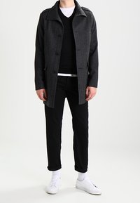 Abrigo de mezcla de lana gris con cuello y cierre de botón, acompañado de un suéter negro, pantalones negros y zapatillas blancas. Diseño sencillo, corte entallado.