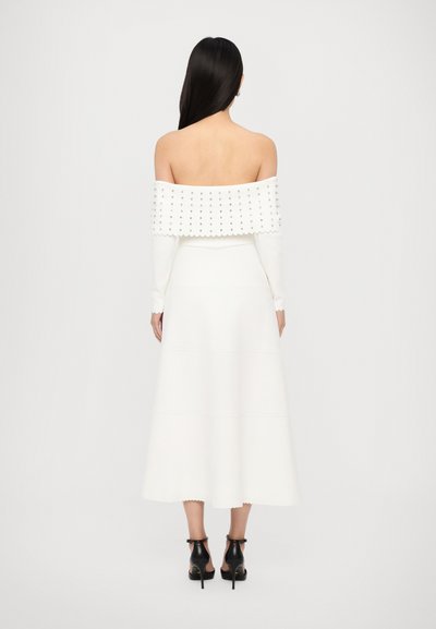 Off-the-shoulder witte jurk met gestikte details, golvende zoom en korte mouwen. Kenmerkt zilveren studs langs het lijfje.