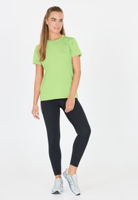 Ljusgrön sportt-shirt med korta ärmar, kombinerad med svarta leggings. Modellen bär ljusgrå löparskor. Slät tyg, figurnära design.