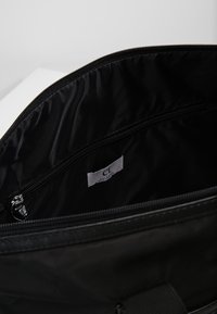 Zwarte tas interieur, gladde textuur, met een ritszak en een stoffen label. Gevoerd met een mat zwarte stof, met een eenvoudig ontwerp.