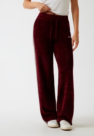 Pantaloni da jogging in velluto bordeaux con vestibilità rilassata, caratterizzati da strisce laterali, vita elasticizzata, cordoncino e tasche frontali. Accentuati da logo.