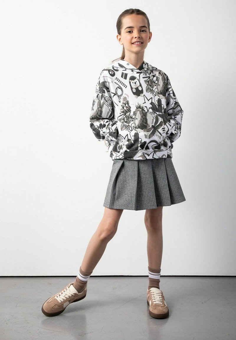 Bluza z kapturem z czarno-białymi wzorami graficznymi, w połączeniu z plisowaną szaro-skalną spódnicą. Brązowe sneakersy z białymi akcentami i pasiastymi skarpetkami.