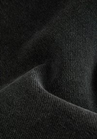 Gros plan sur un tissu noir tricoté montrant un tissage texturé et de légers plis dans le matériau.