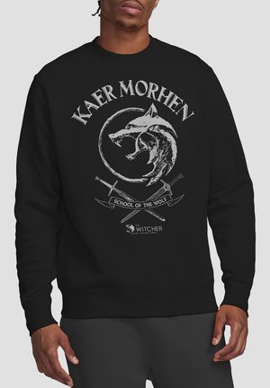 Schwarzer Kapuzenpullover mit einem zirkulären Wolfsmotiv und gekreuzten Schwertern, mit dem Text "KAER MORHEN" und "SCHULE DES WOLFES" in Weiß.